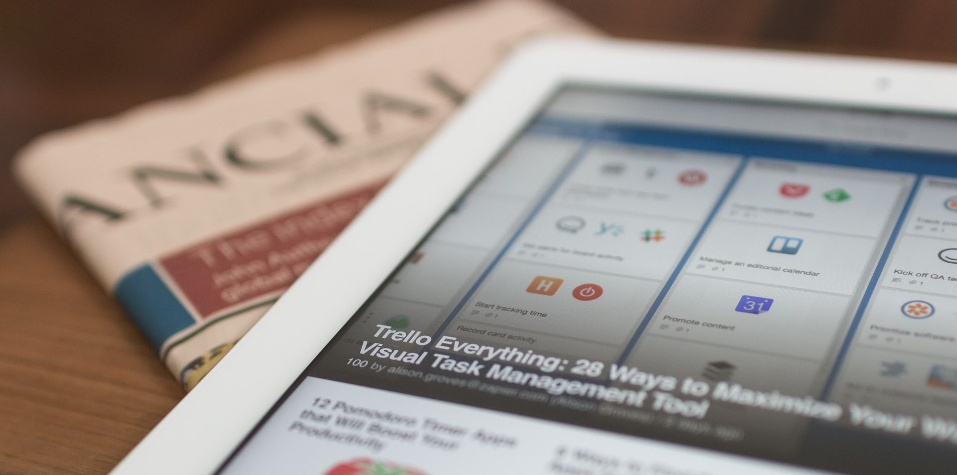 A close up shot of a digital news headline on an tablet next to a paper news paper
