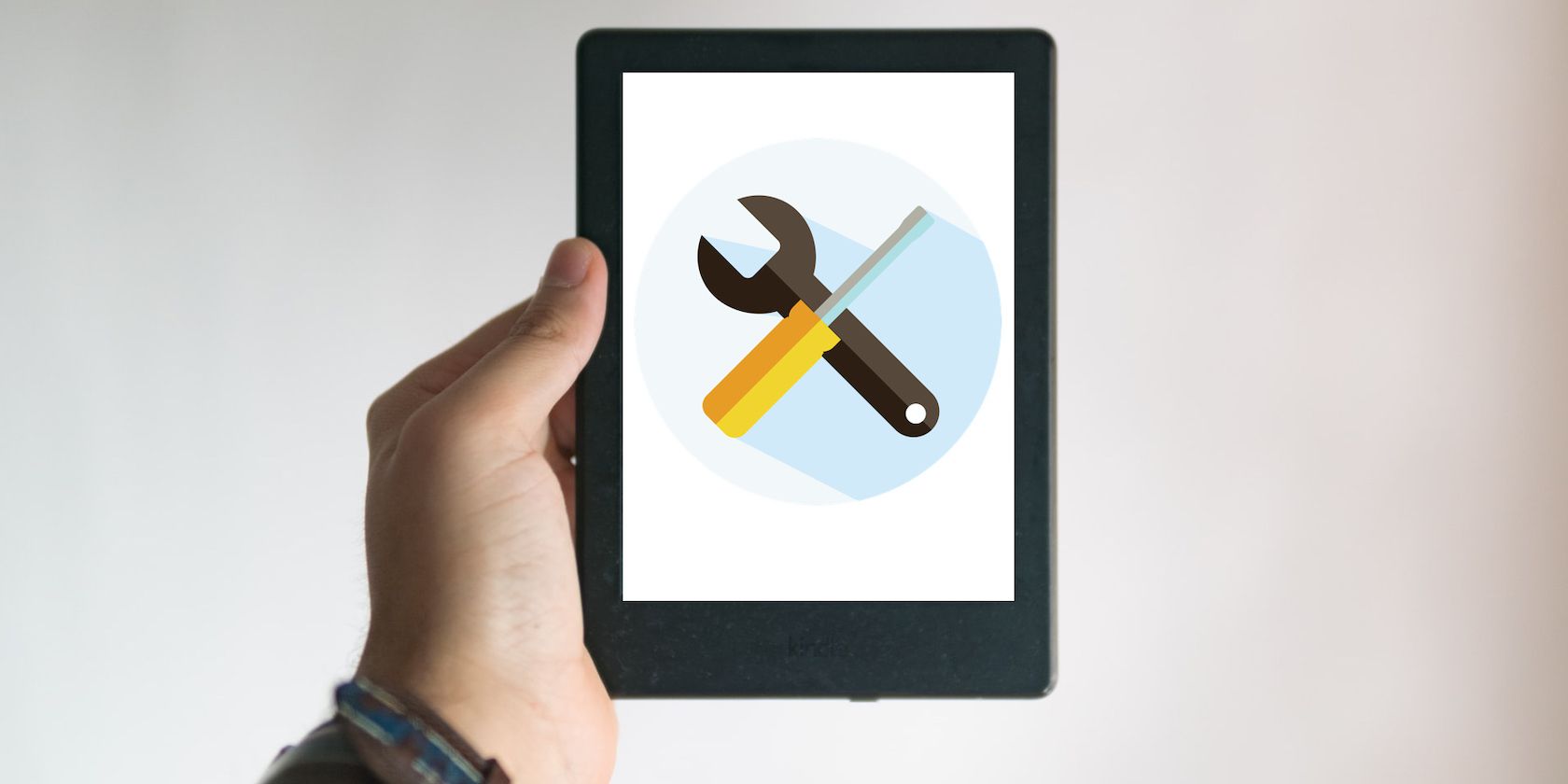 A close up of a hand holding up a Kindle with a screwdriver and cogwheel logo overlaid