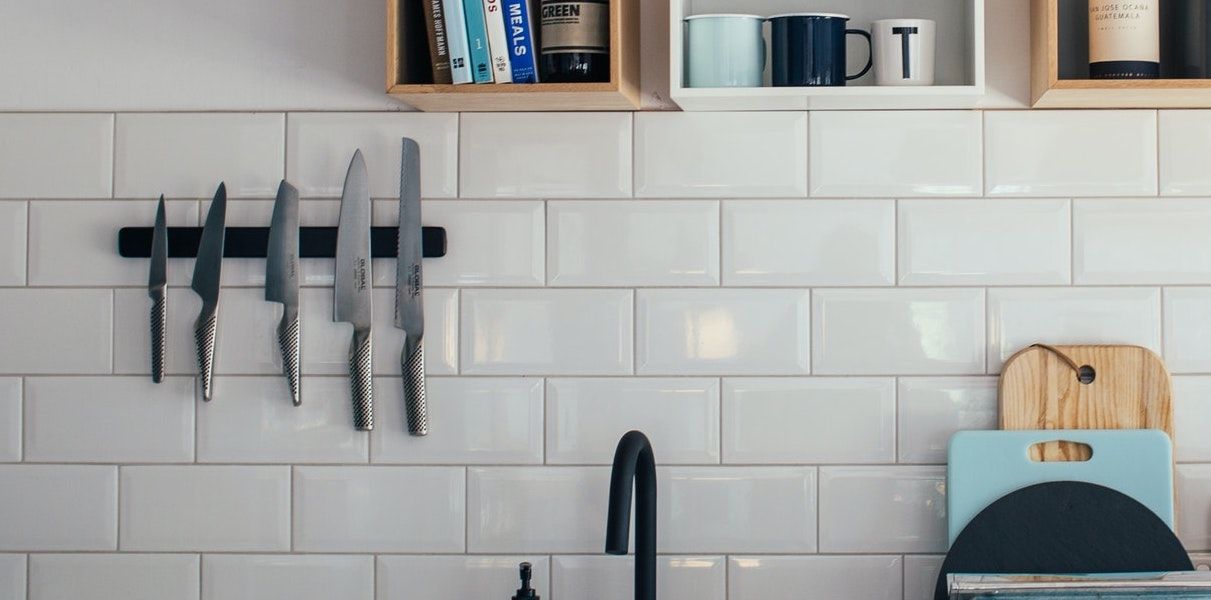 A magnetic knife block with knives on a white tiled kitchen wall