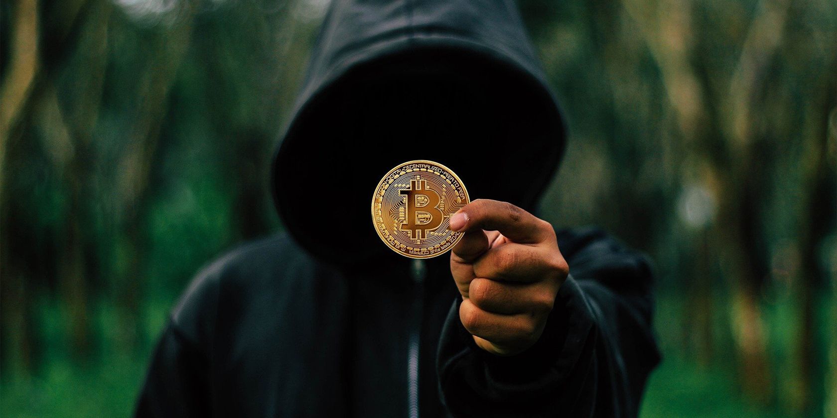 hooded person holding a bitcoin for robbery