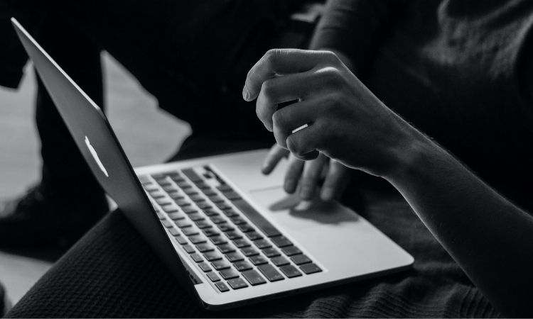 greyscale photo of man sitting using mac laptop