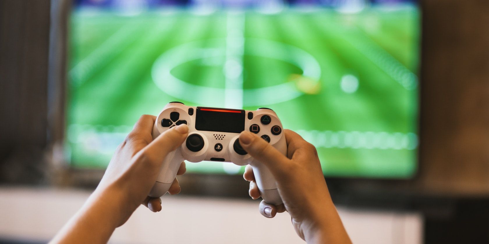 A pair of hands holding a game console in front of a television