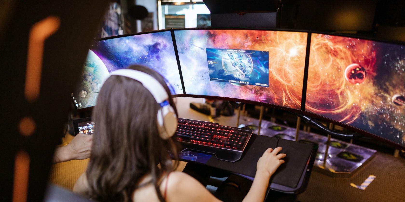 A woman with headphones on playing a video game in front of a desktop