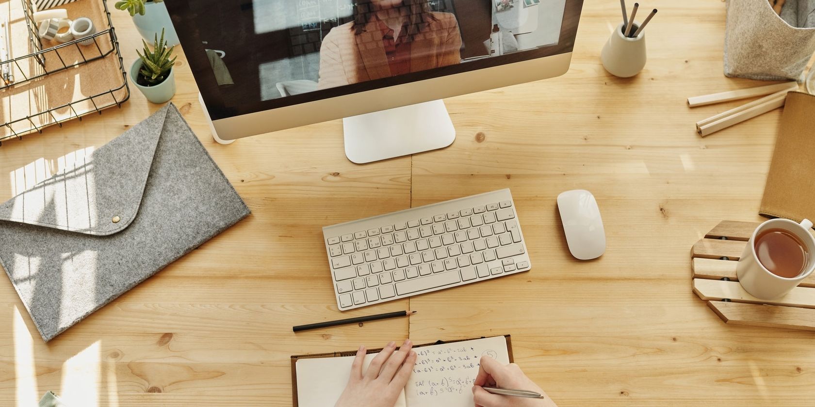 iMac on desk during FaceTime call with hand holding pen and writing in notebook.