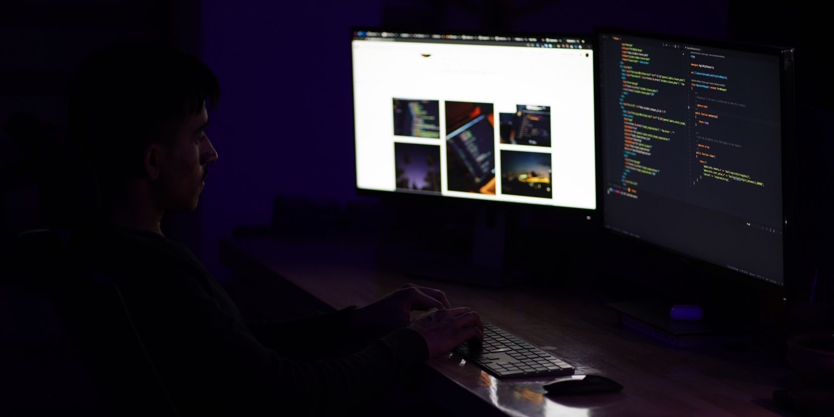 man in a dark room with purple backlighting at a desk typing on his computer