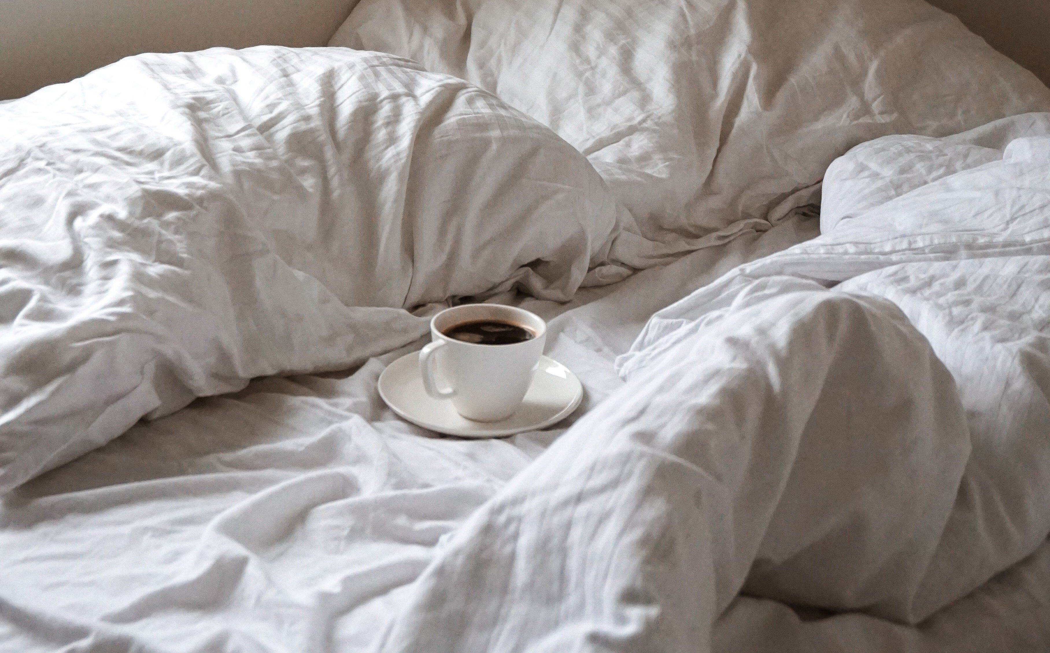A cup of coffee in an unmade bed.