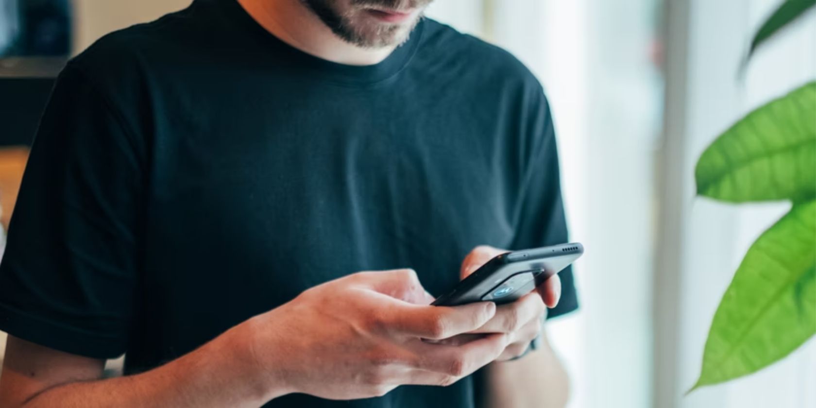 man holding and looking down at smartphone indoors