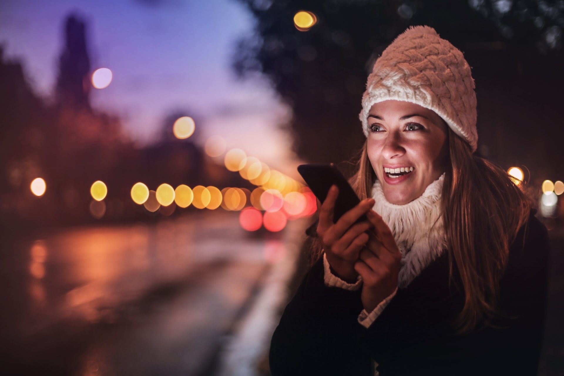 Woman with phone along a street at night
