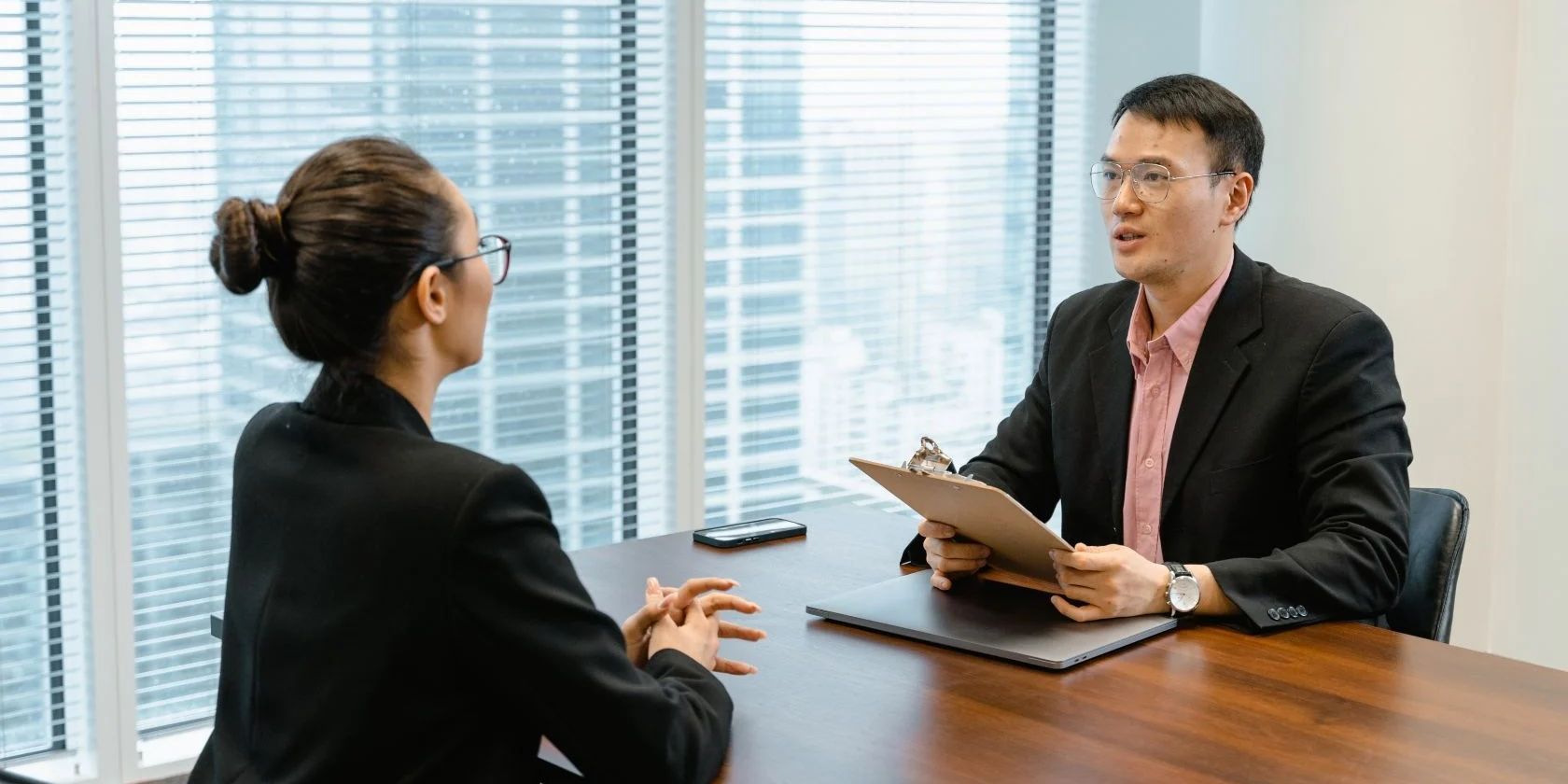 A man interviewing a woman sitting across the table.