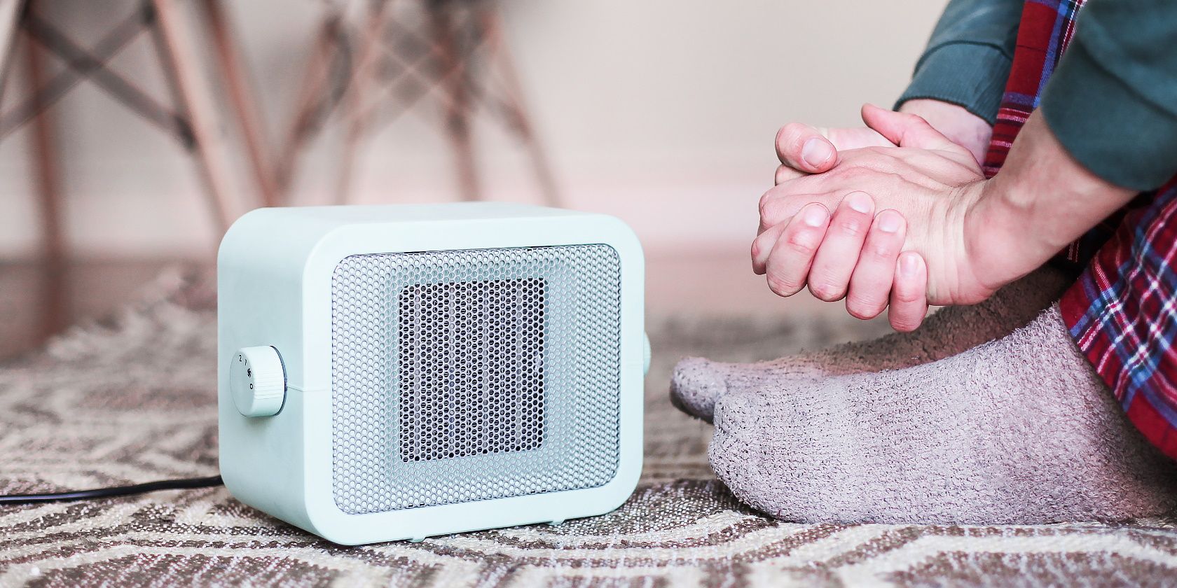 A blue heater on the carpet in a cosy room. A man in pyjamas warming his hands next to the heater