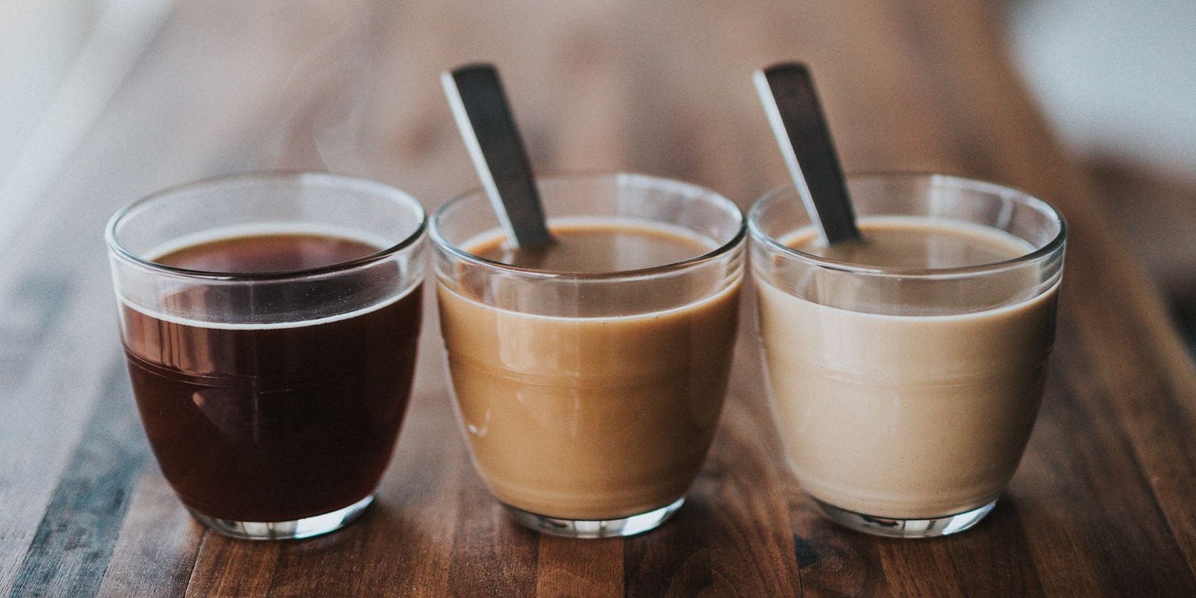 Three espressos lined up on a wood table.