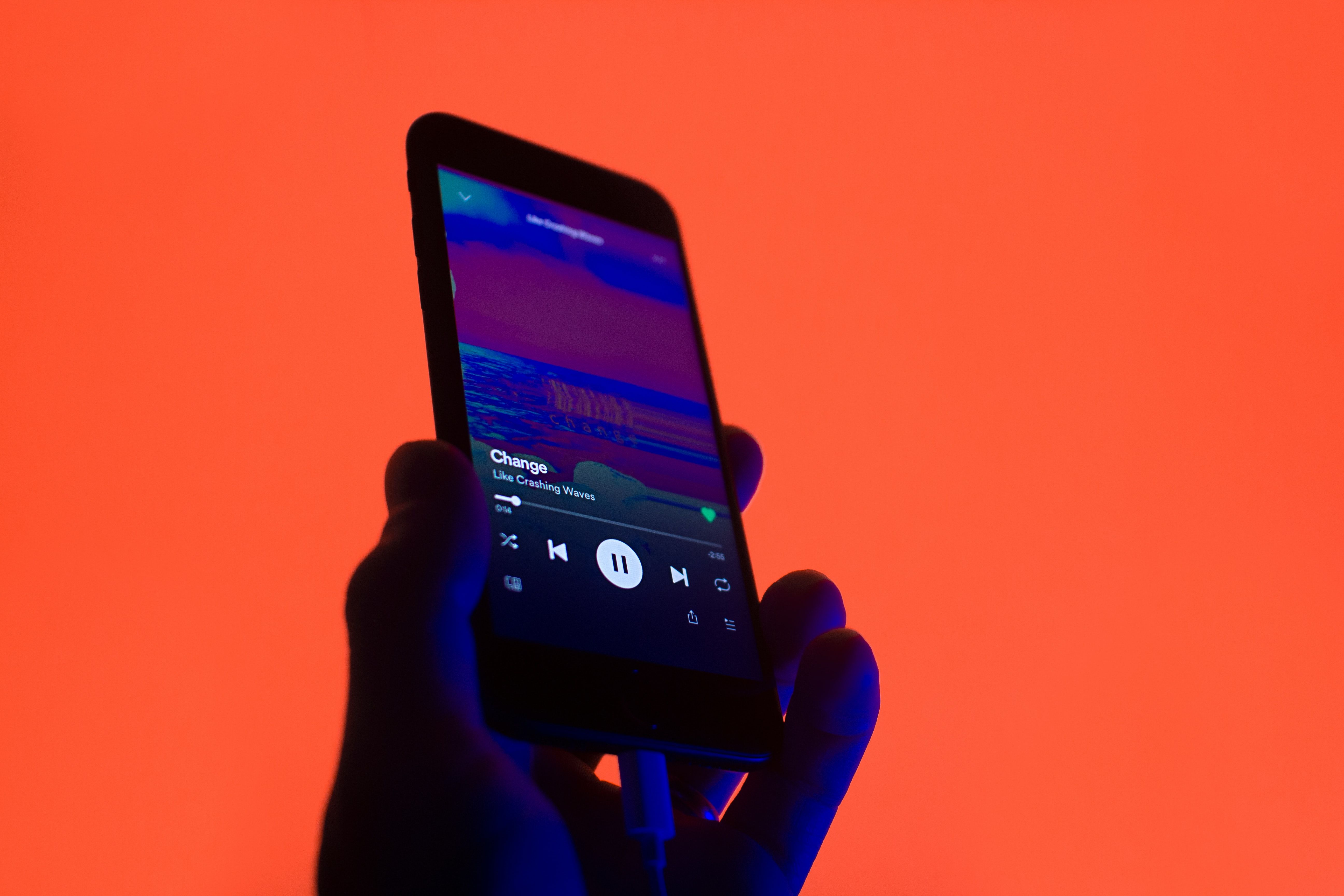 A person playing music on a smartphone over red.