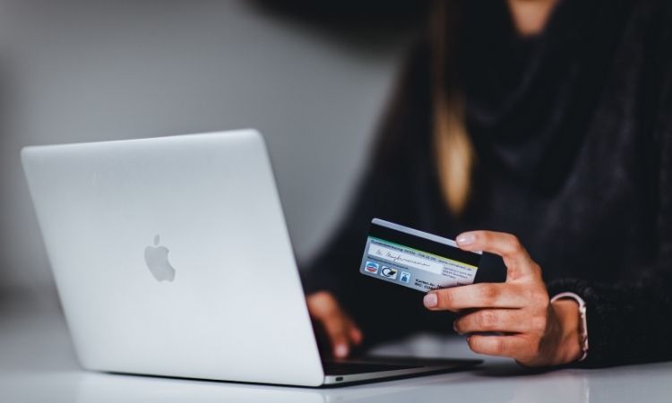 woman holding a credit card while sitting at desk on Mac laptop