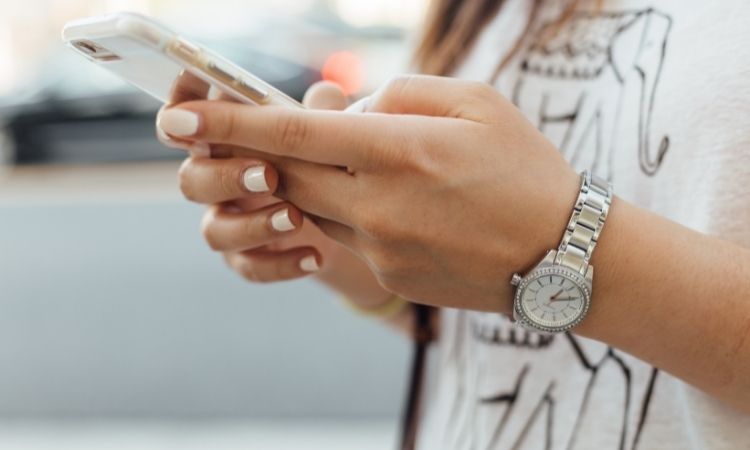 woman with white painted nails and watch outside holding phone