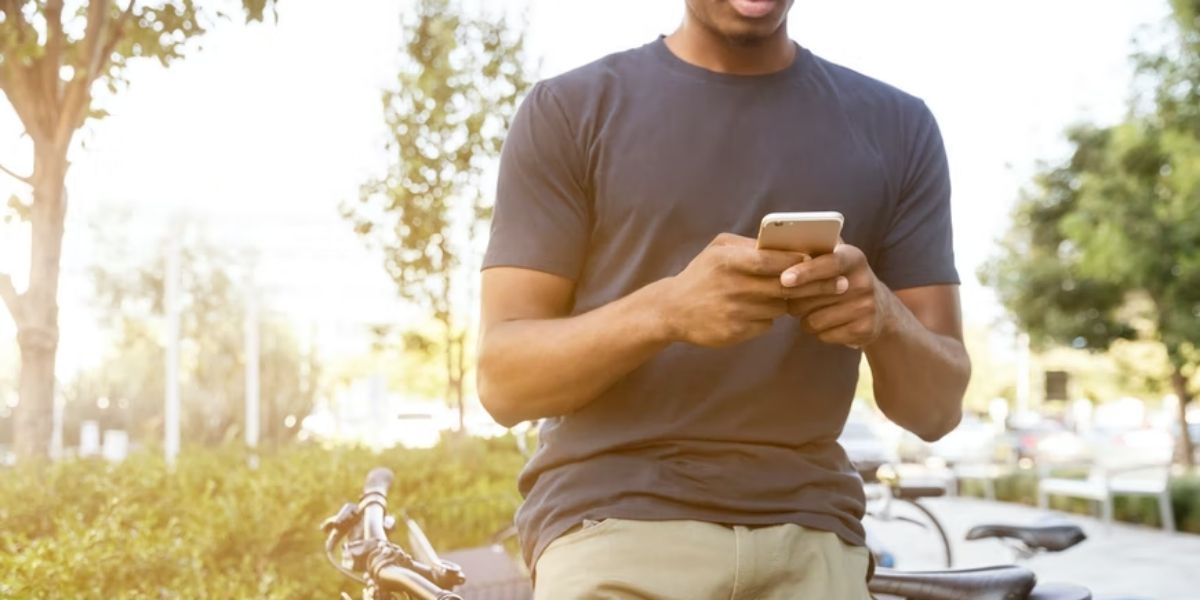 man using smartphone while sitting on bicycle in park