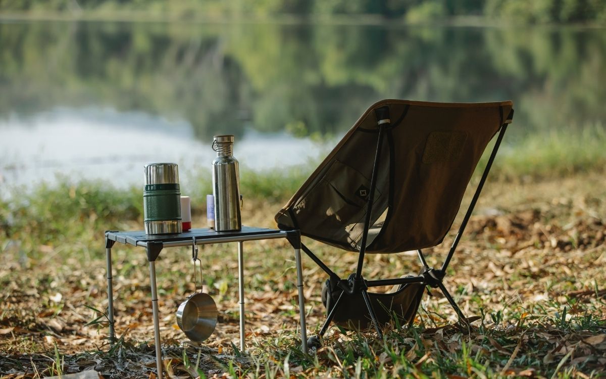 Cadeira de acampamento com uma garrafa de água inteligente em cima da mesa perto da margem do rio