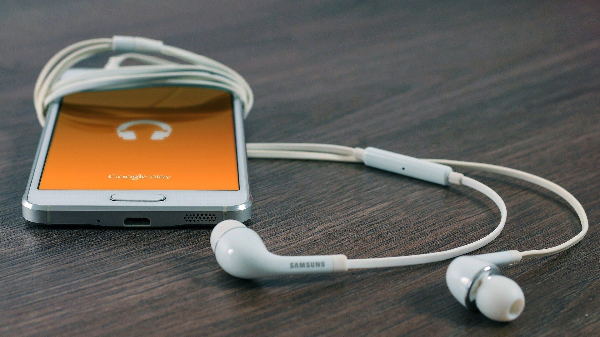 Google play music pulled up on a samsung smartphone with earbuds laying near it