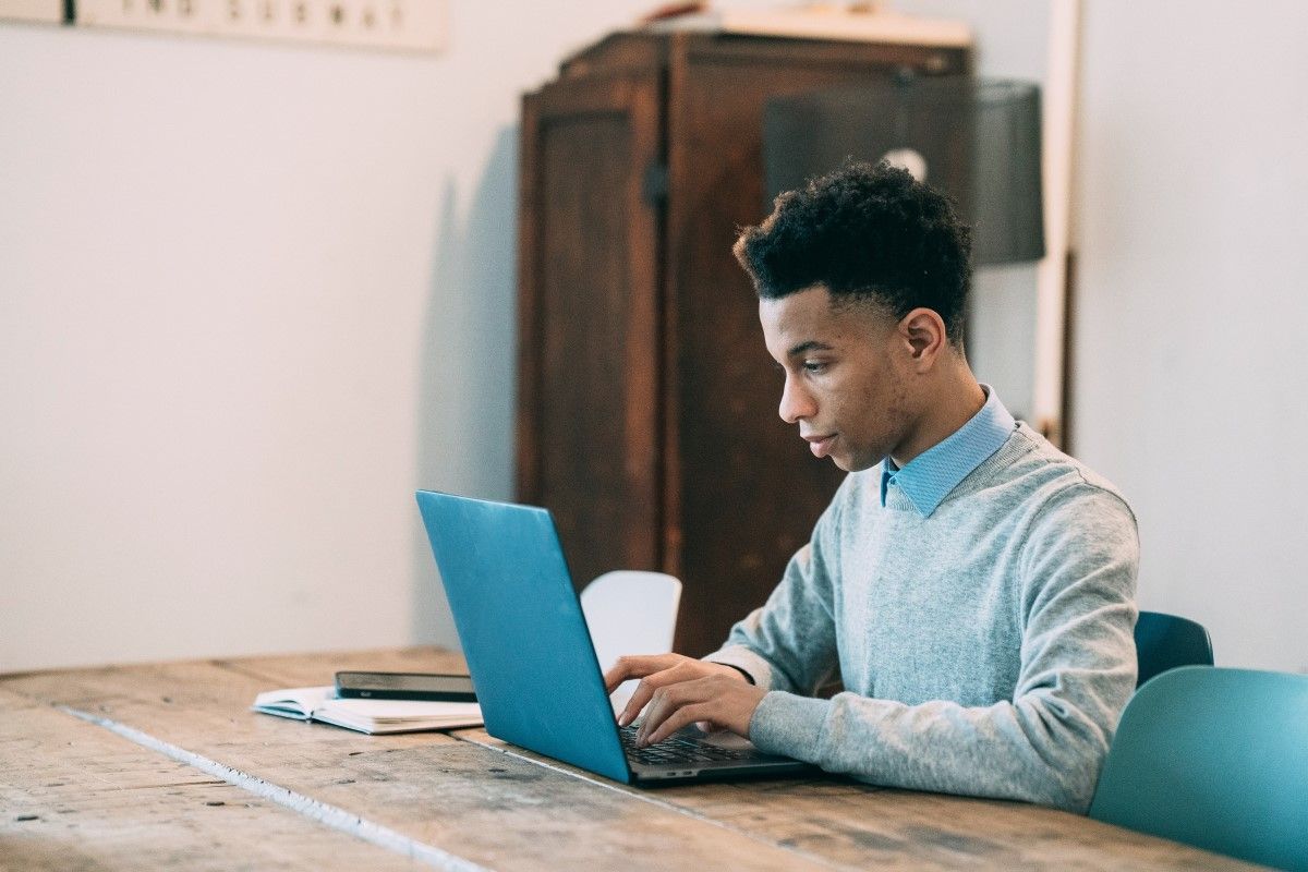 A young black man is sitting at a table on a laptop working