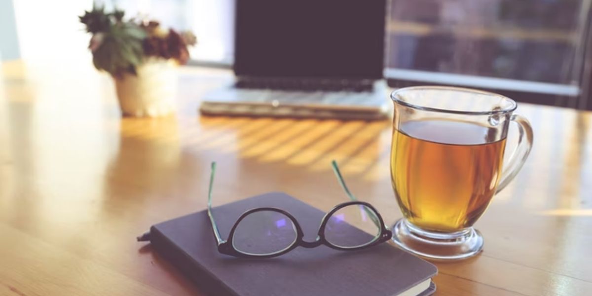 cup of tea on wooden table, next to a pair of glasses and a book