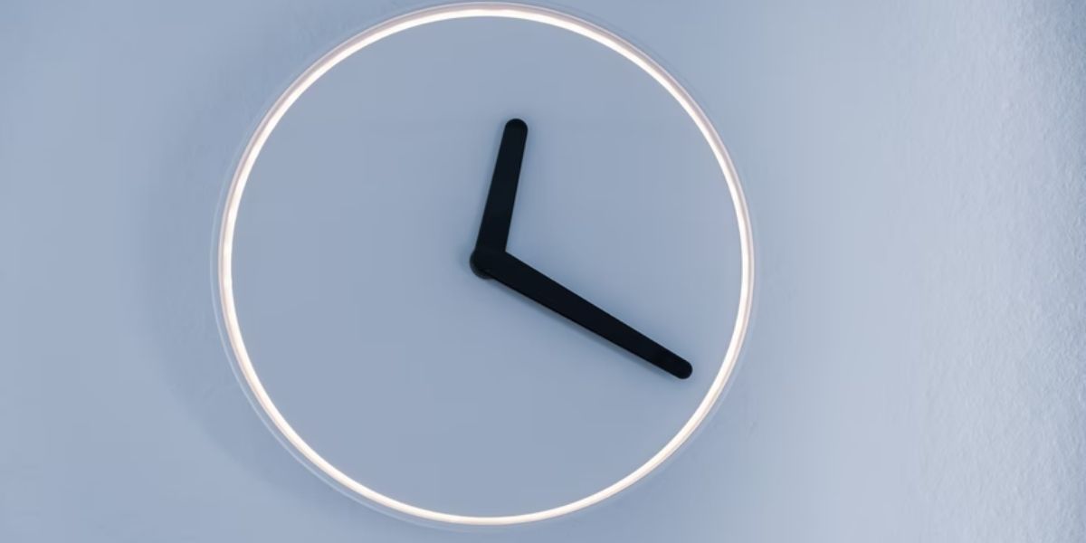 minimalist clock with white edge and black hourly and minute hands on light blue wall