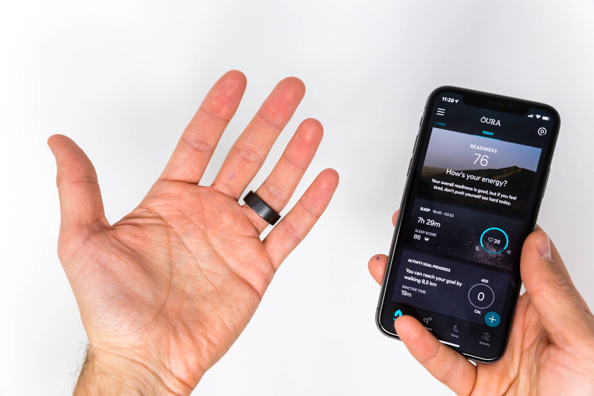 A hand wearing the Oura smart ring next to a phone displaying the Oura app metrics