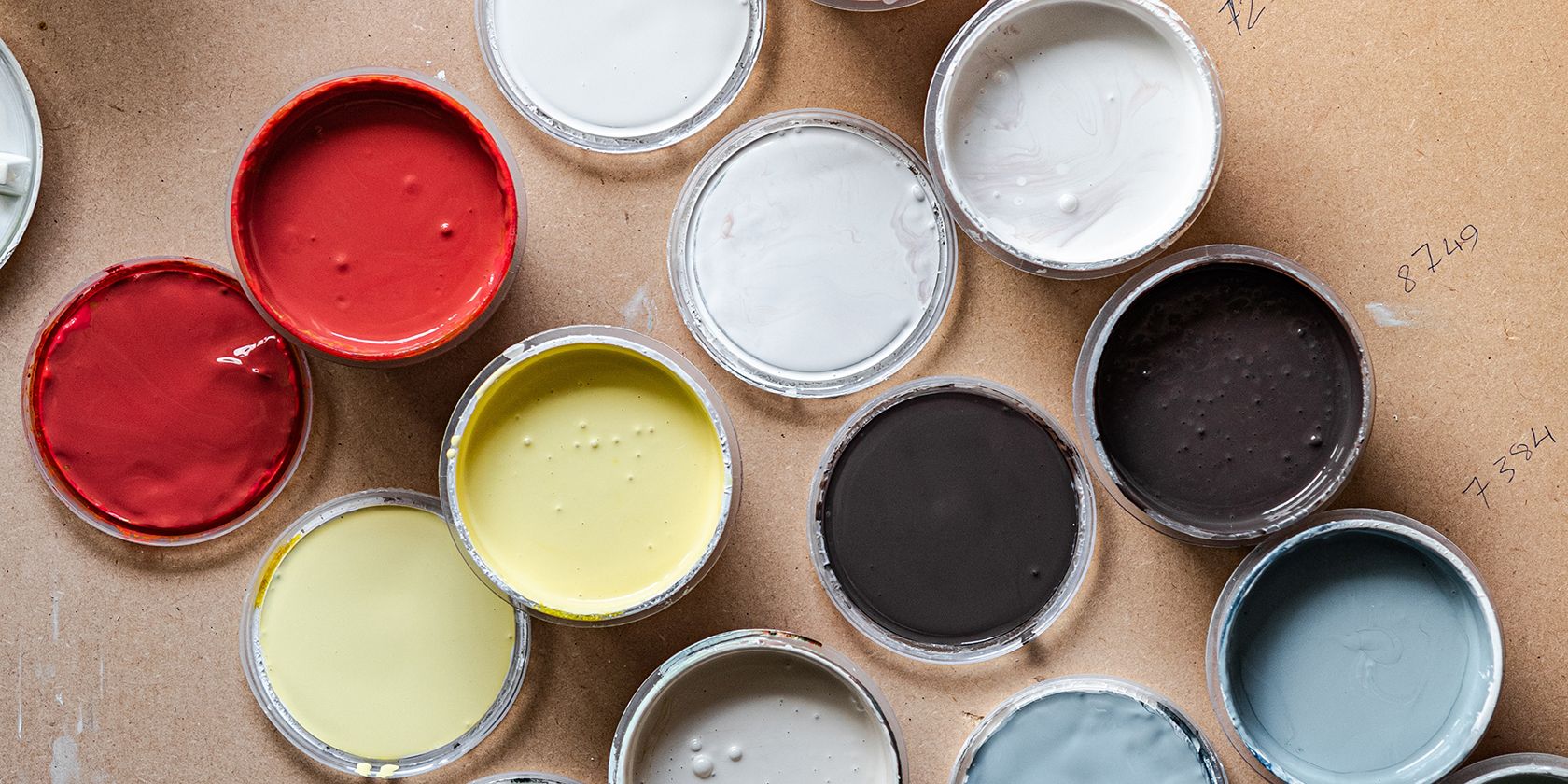 Bird's eye view of open paint cans with their lids next to them, showing different color paint from red, pastel yellow, and shades of gray.
