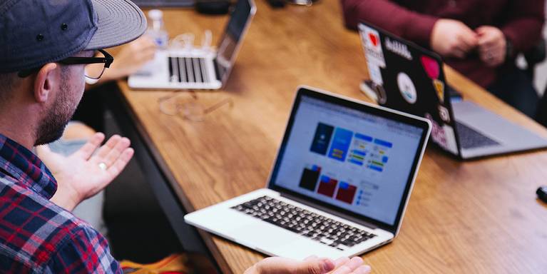Foto seorang pria melihat laptop yang menunjukkan desain UX/UI di layar.