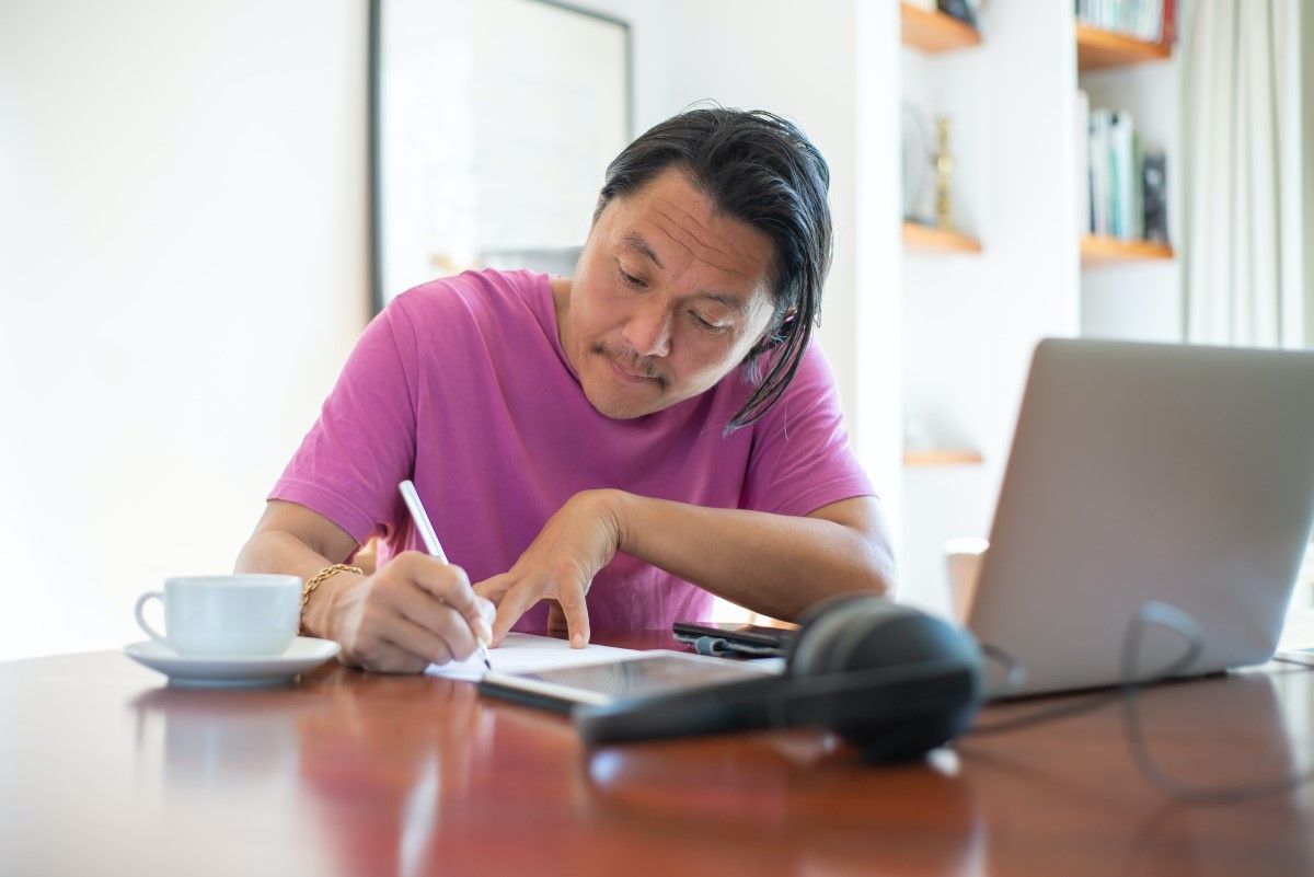 An Asian man sitting at a table and taking notes