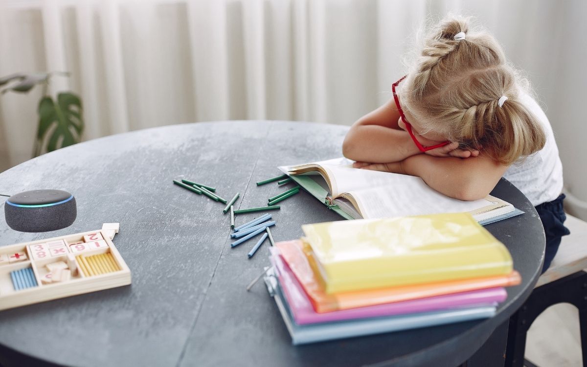 Tired little girl sleeping on book at home and Echo device on table