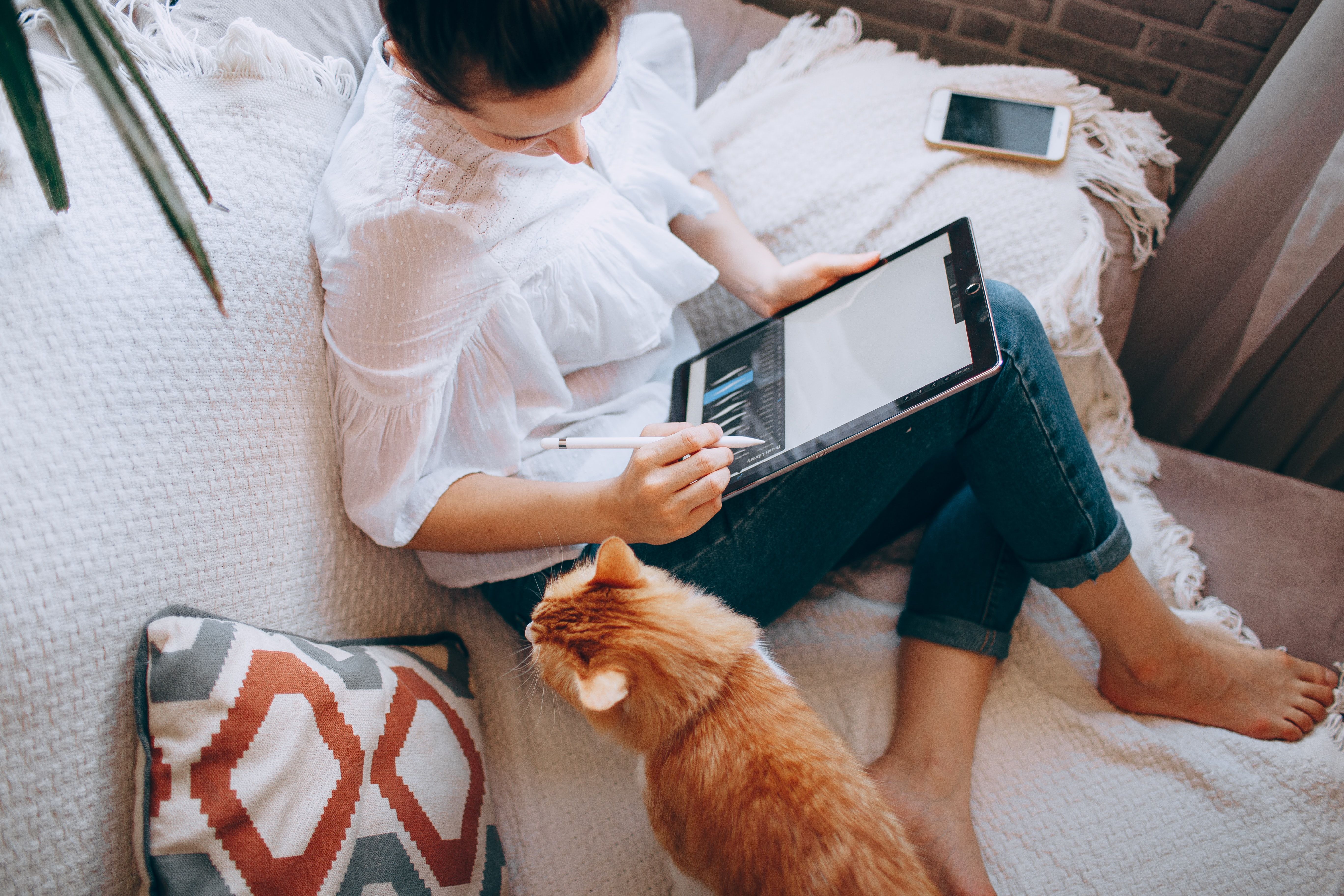 Woman working from home on a tablet with a cat for company.