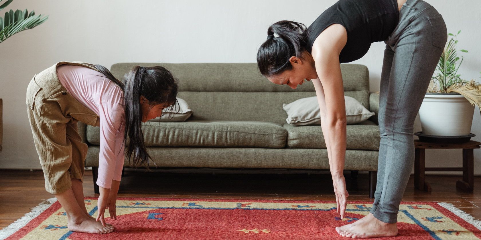 woman and little girl stretching to touch their toes in living room