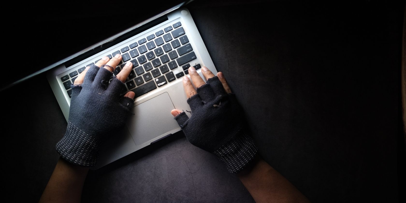 hands in black fingerless gloves typing on a laptop in a dark room