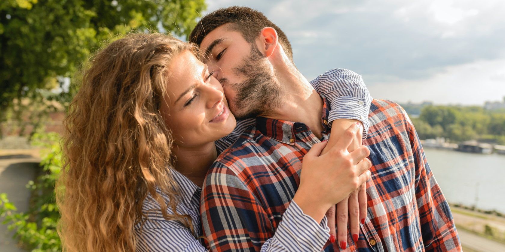 Happy woman embracing man while he kisses her cheek