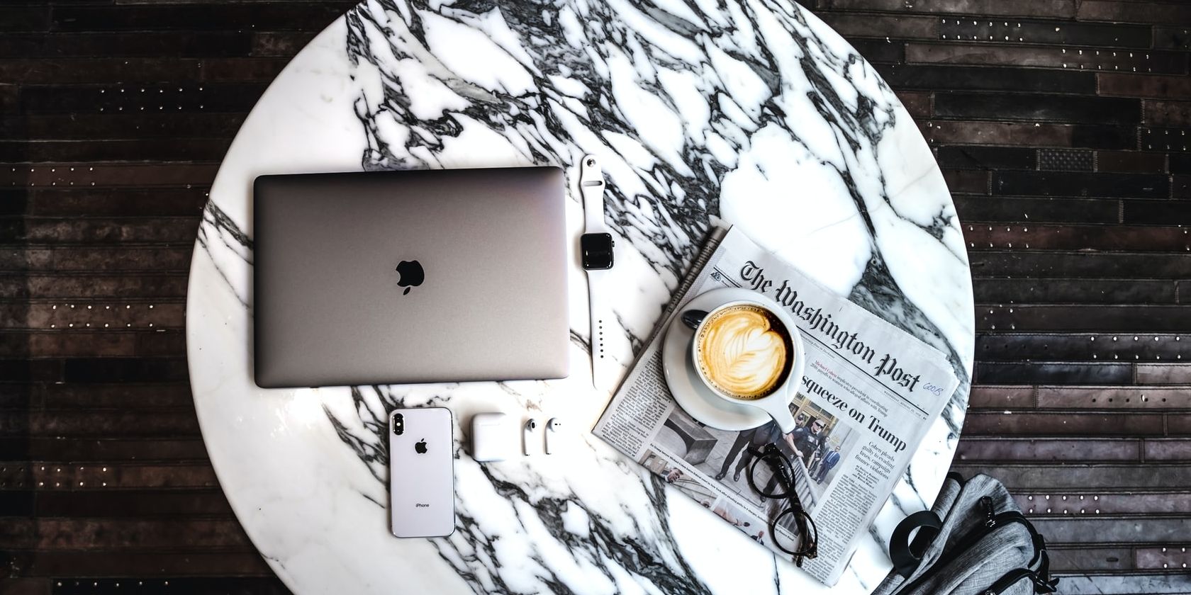 Macbook sitting on round marbled table with a newspaper and other items.