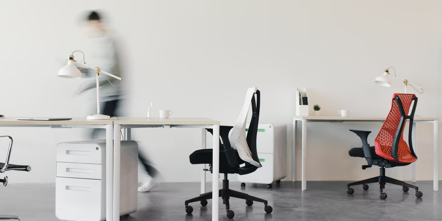A person walking through a modern, minimalist office of chairs and desks