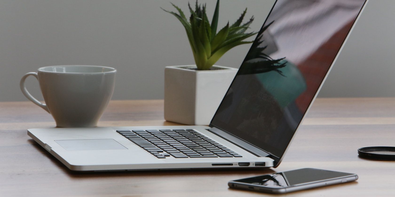 A sleek-looking laptop on a table next to a plant, mug, and mobile phone