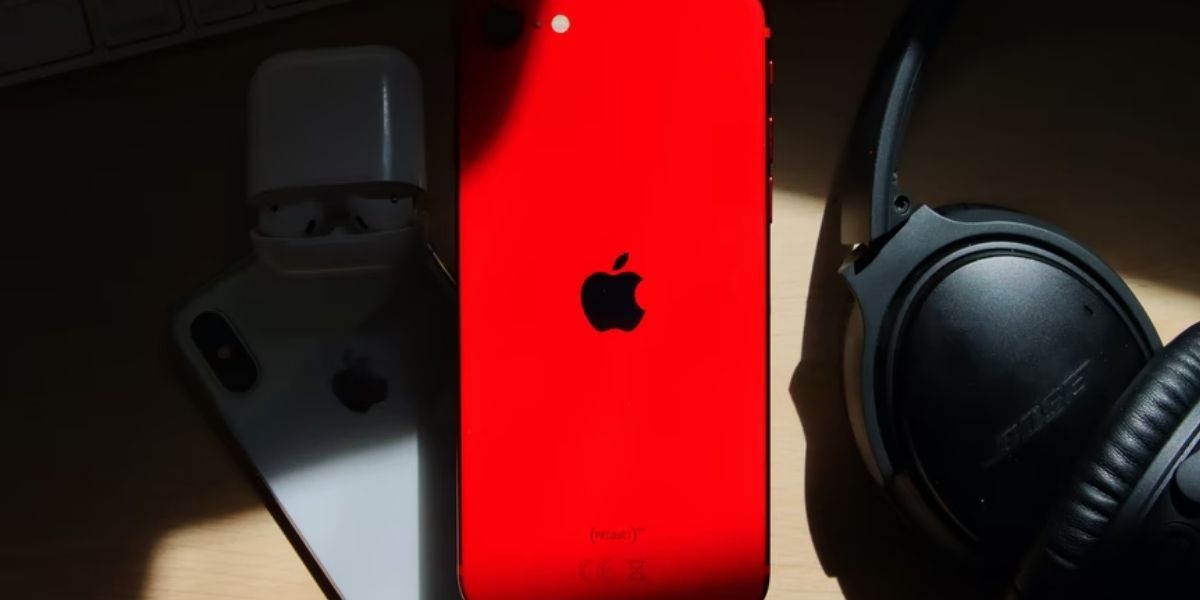 red iphone 7 next to black headphones on wooden desk