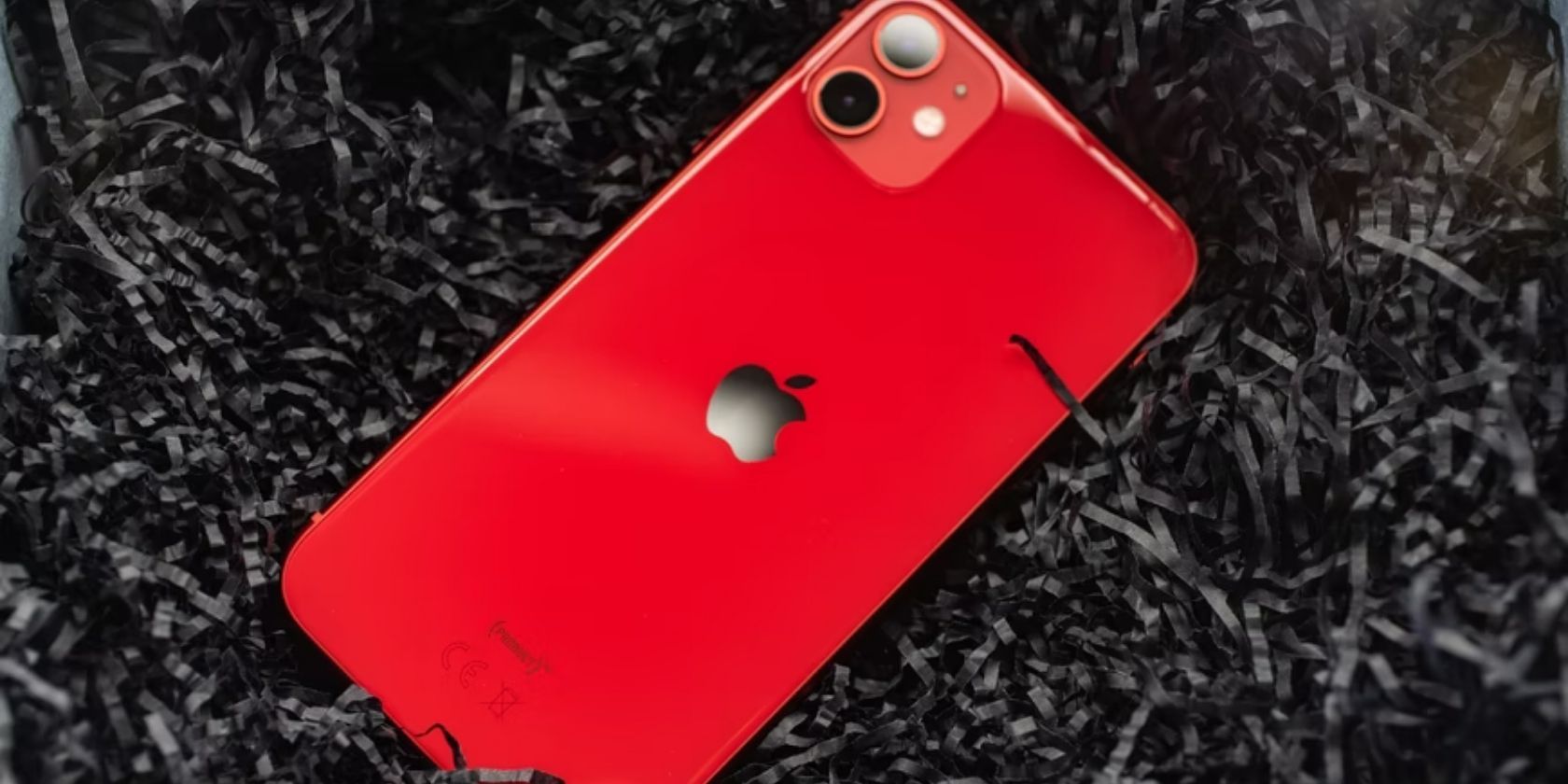 red iphone placed on black crinkle paper shreds