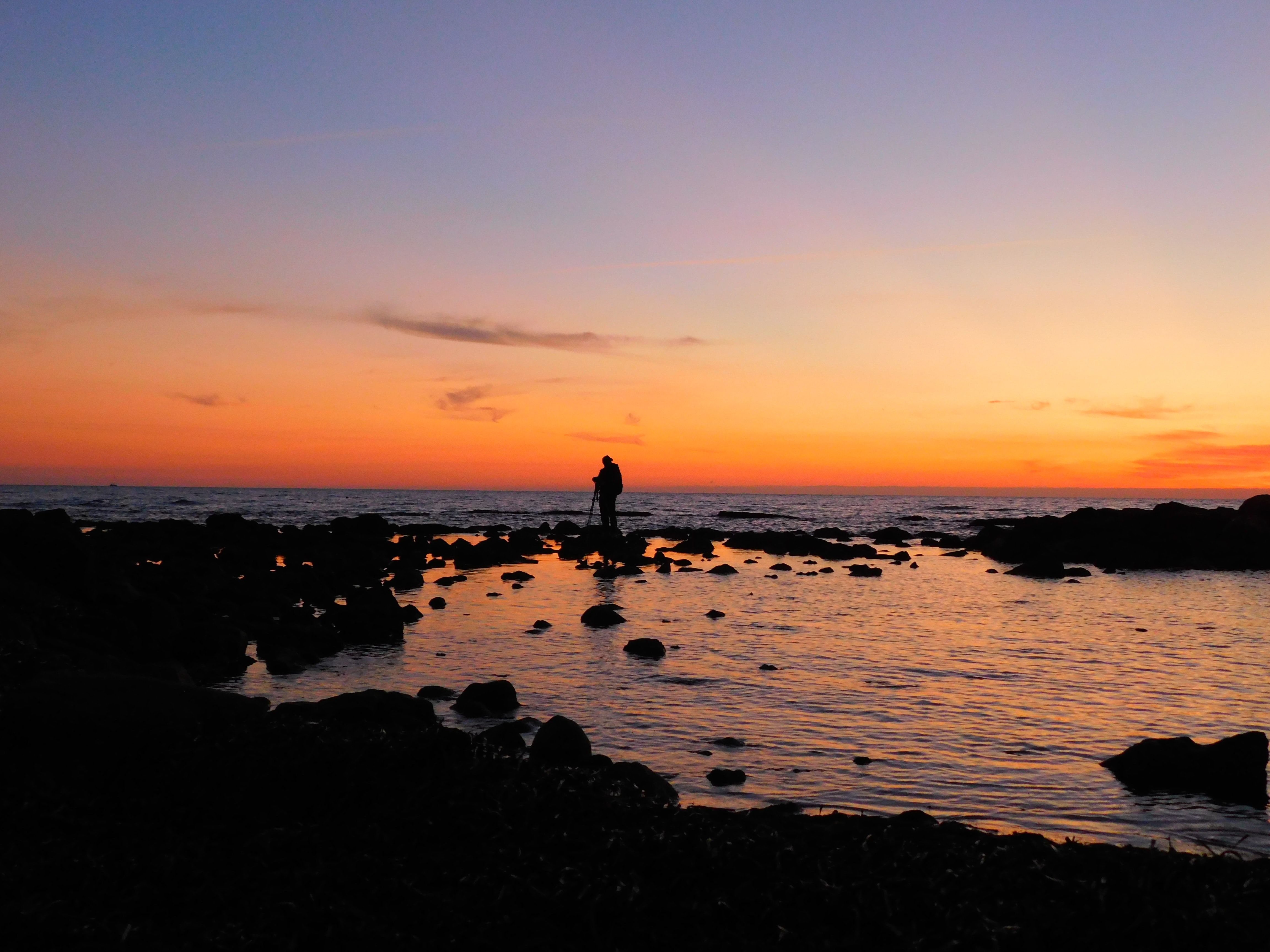 A person walking along the shore at sunset.