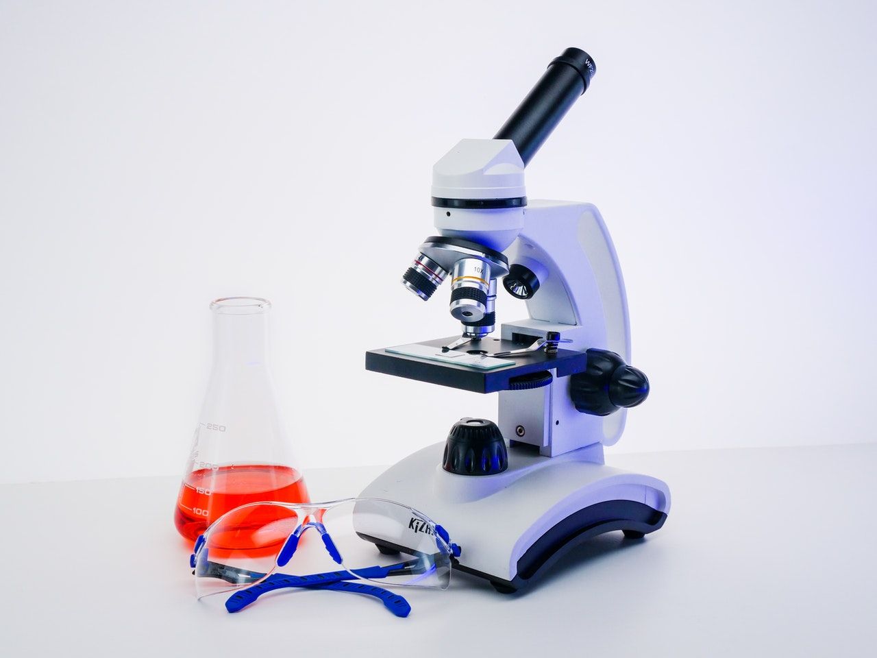 traditional microscope on white background with beaker and safety glasses