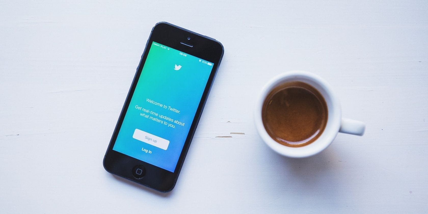 A phone with the Twitter app open next a cup of coffee