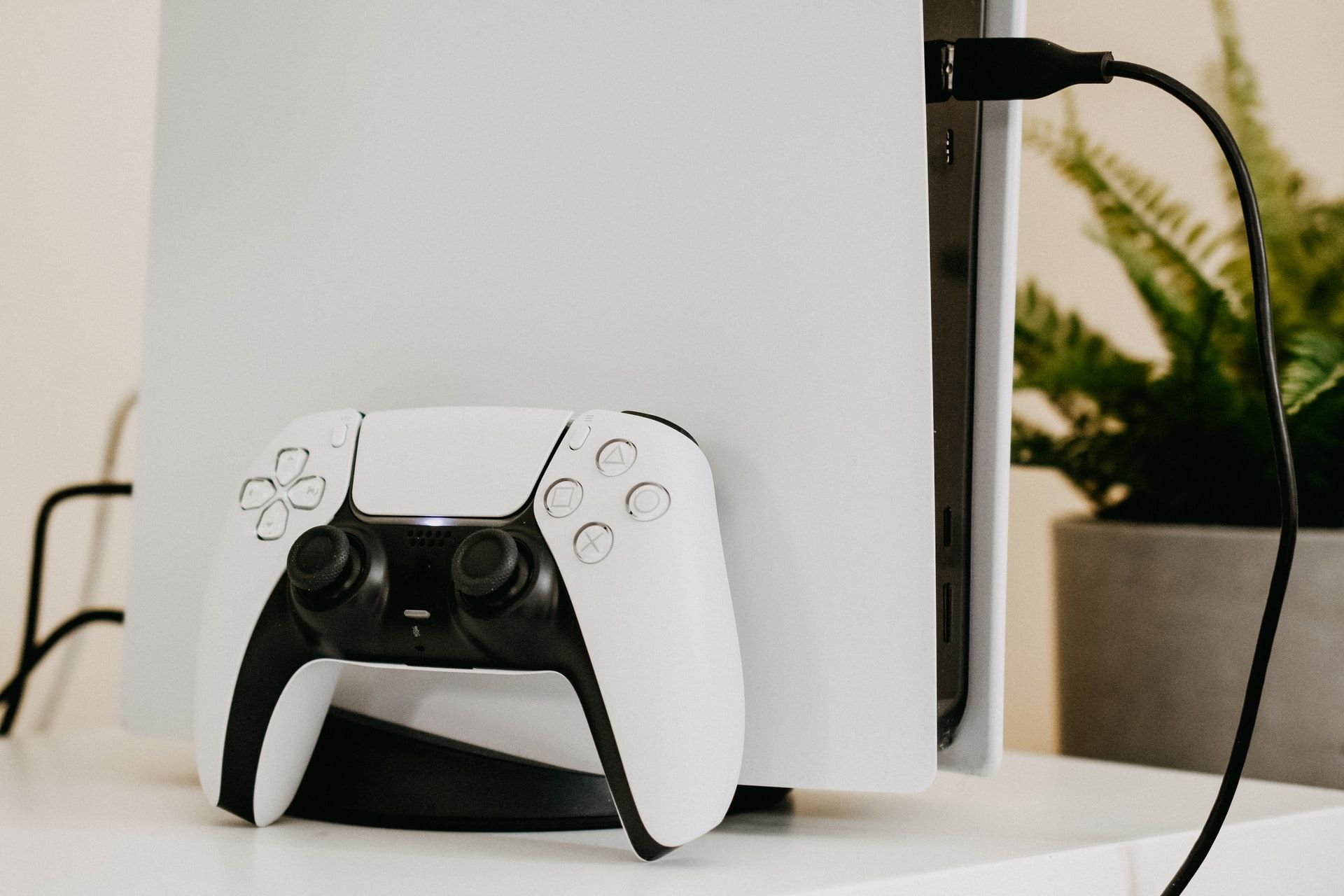 white ps5 playstation 5  with controller on desk with plant in background