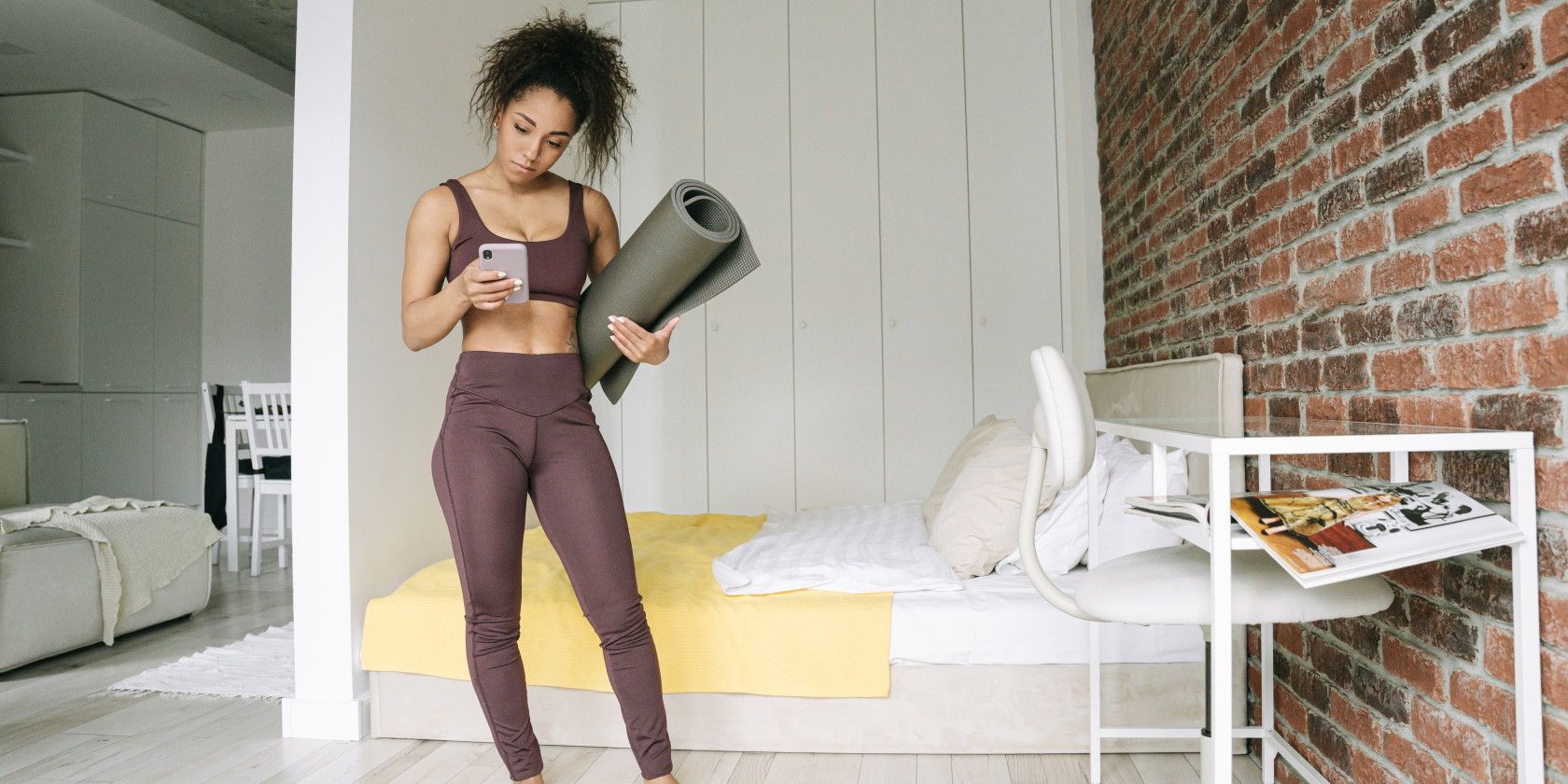 woman standing in bedroom holding exercise mat and using smartphone