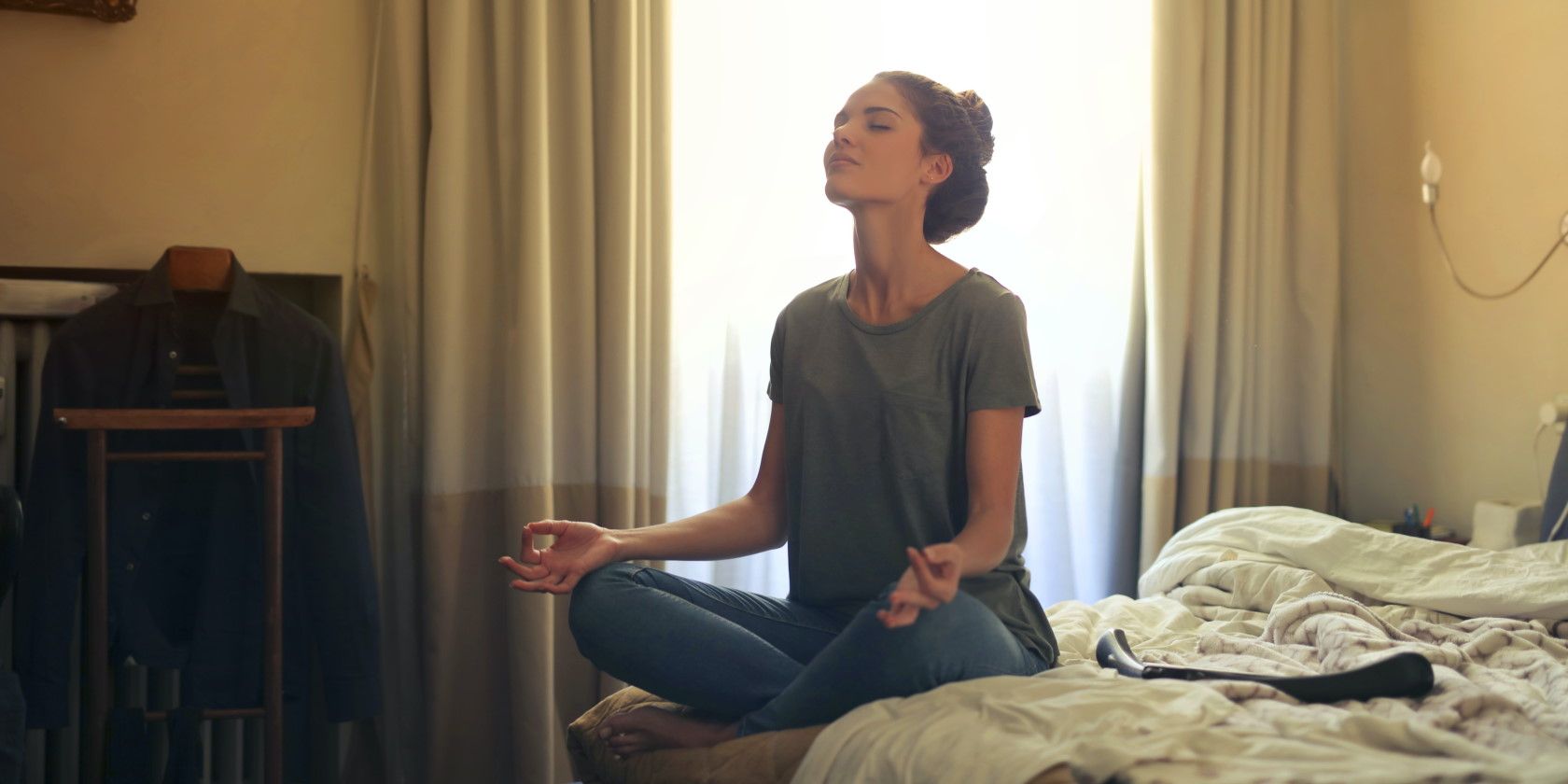 woman sitting on bed with closed eyes and meditating