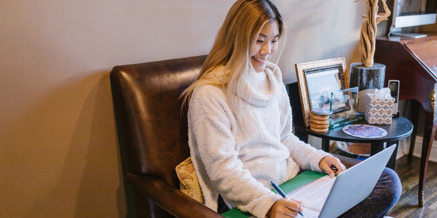 Femme assise sur une chaise, prenant des notes et utilisant un ordinateur portable.