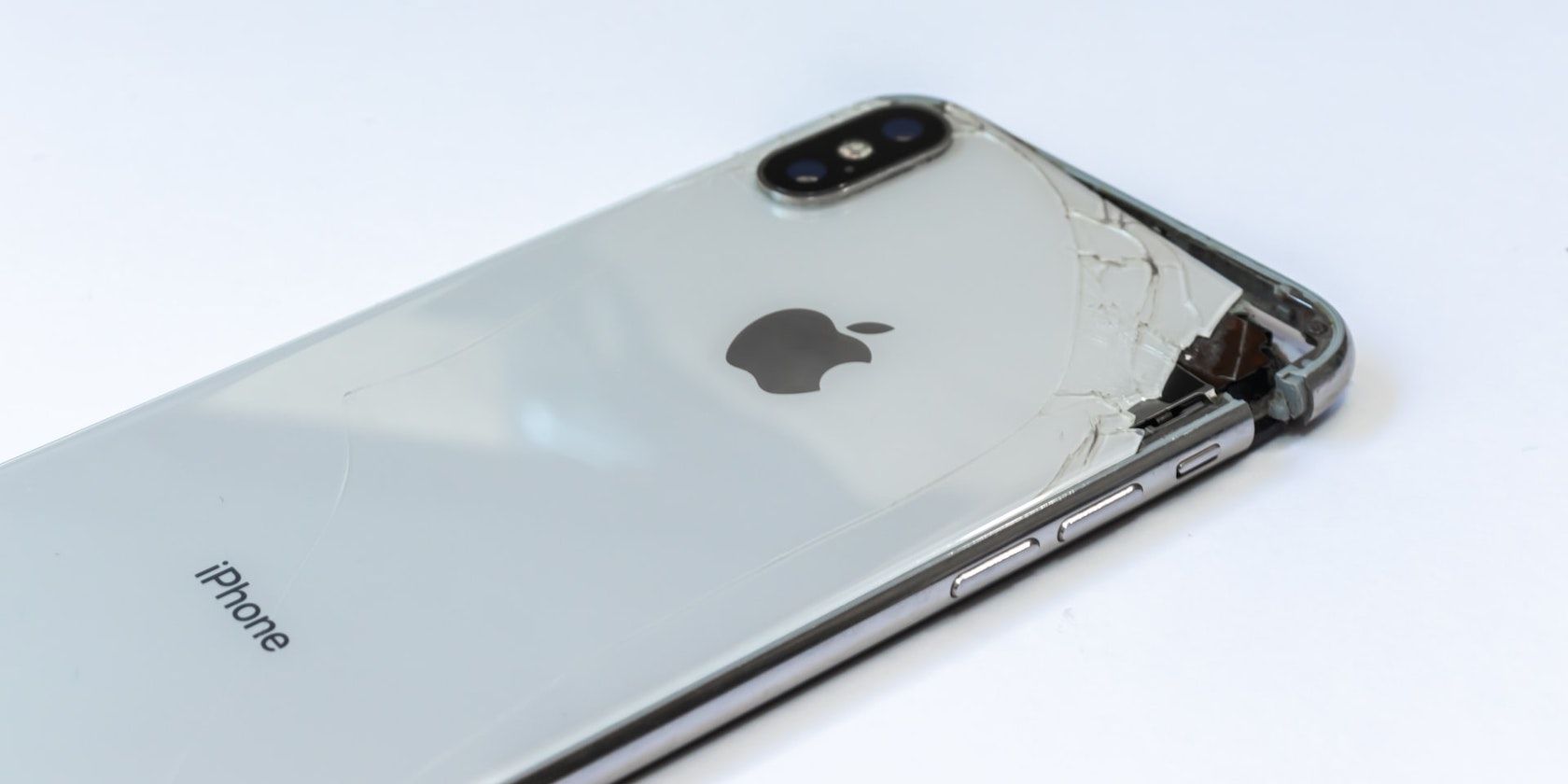 A close up of a broken silver iPhone on a plain white background