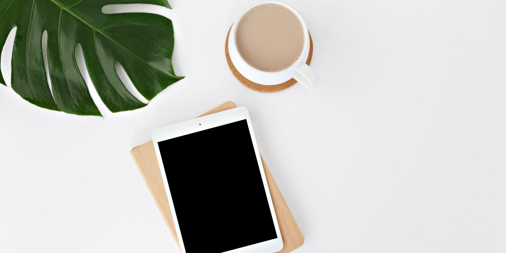 A tablet, a plant, and a cup of coffee on a desk