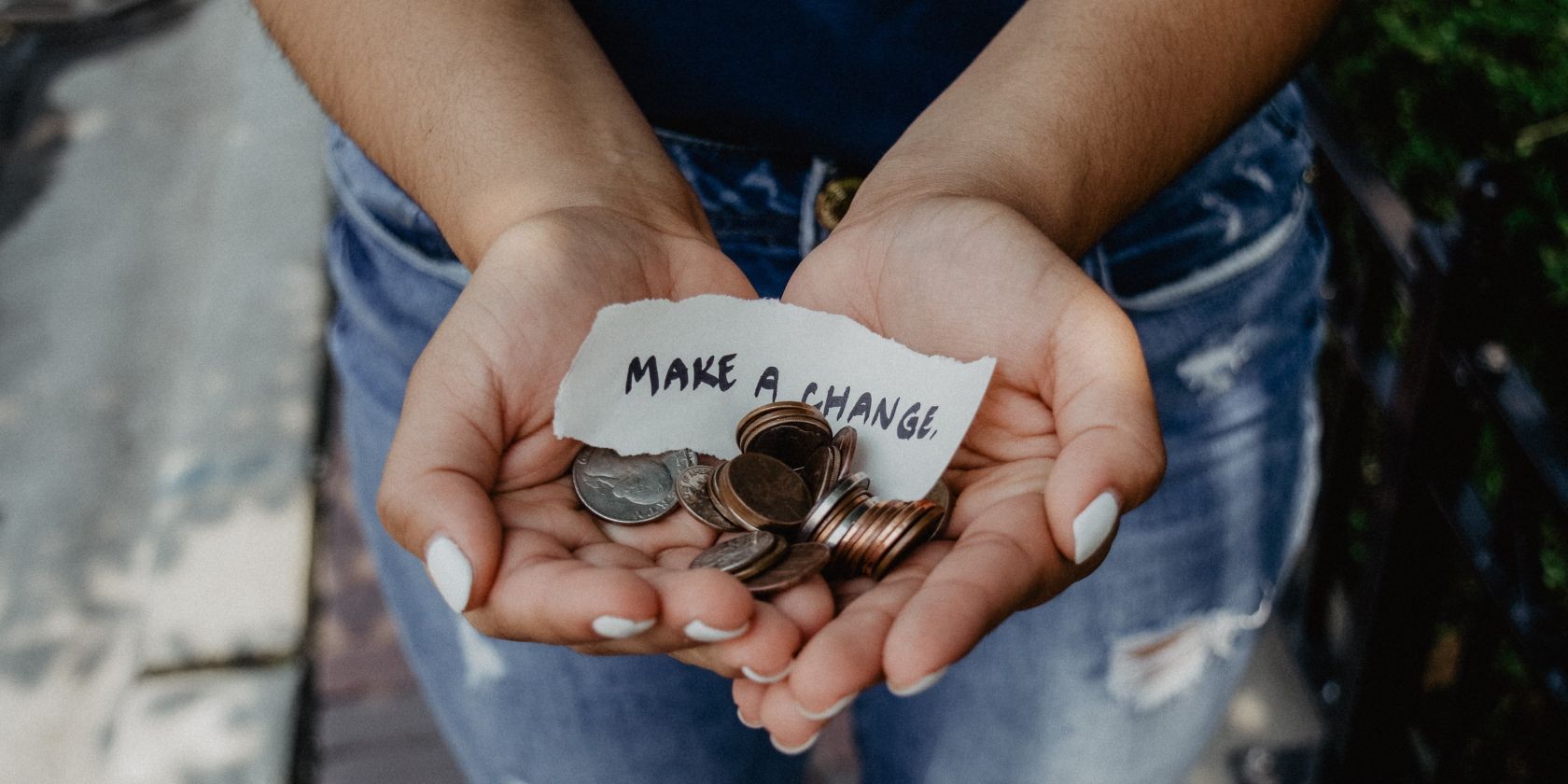 Two Hands Holding Coins and a Note That Reads "Make A Change"