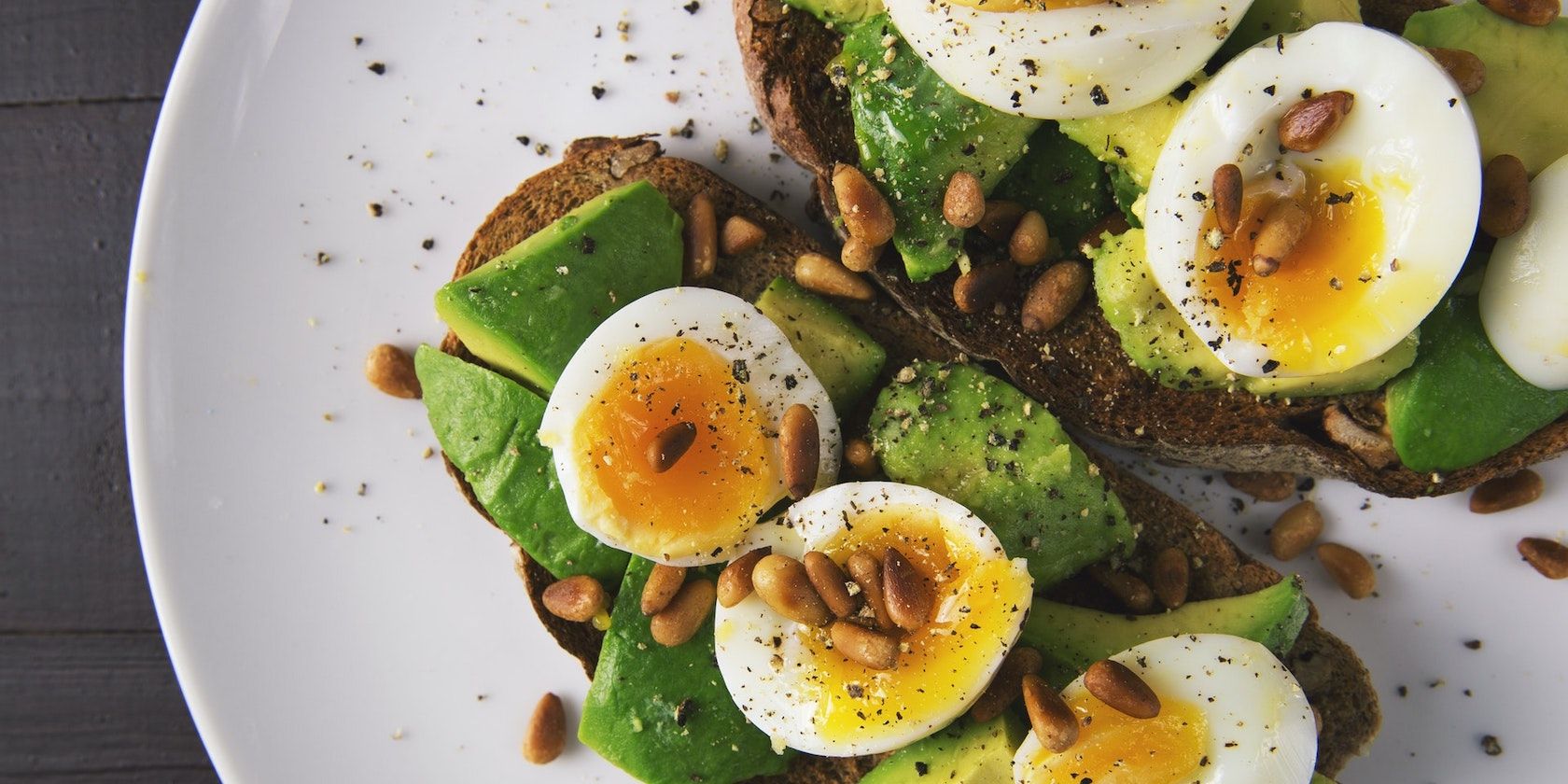 A plate of boiled eggs on toast with avocado