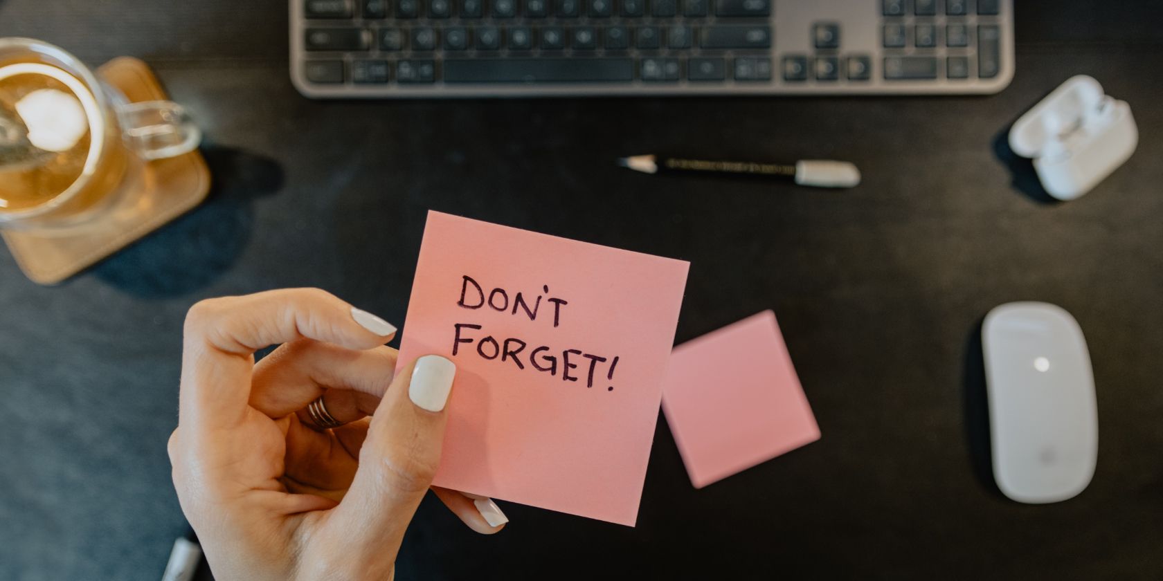 A hand with a sticky note that says don't forget above a computer keyboard